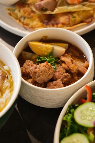 a table topped with bowls of soup and vegetables at Tuong Boutique Resort Mui ne in Mui Ne