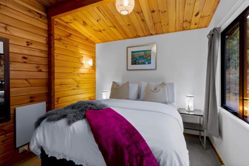 um quarto com uma cama branca e um cobertor roxo em Kereru Cottage, Romantic & Beautiful Log Cabin - Queenstown em Queenstown