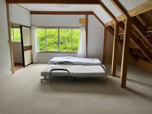 two beds in a room with a window at 大自然の一軒家。便利社会からの逃避、究極のセルフ山小屋ライフ in Madarao Kogen