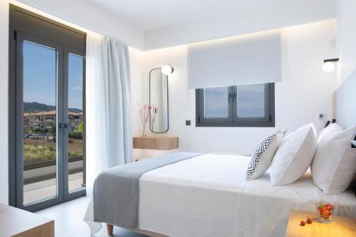 a white bedroom with a bed and a large window at Achillion Suites in Lefkada Town