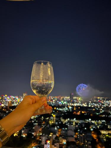a person holding a glass of wine overlooking a city at Luxury Apartment - Rooftop Swimming Pool - Beach Front - Hinata Apartment in Da Nang