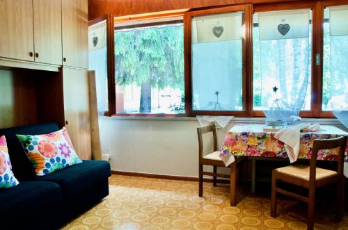 sala de estar con mesa, sofá y ventanas en Al Sole di TSS' - Cozy Apartment a 20 Metri dal Lago di Caldonazzo - Perfetto per coppie a Calceranica al Lago, en Calceranica al Lago
