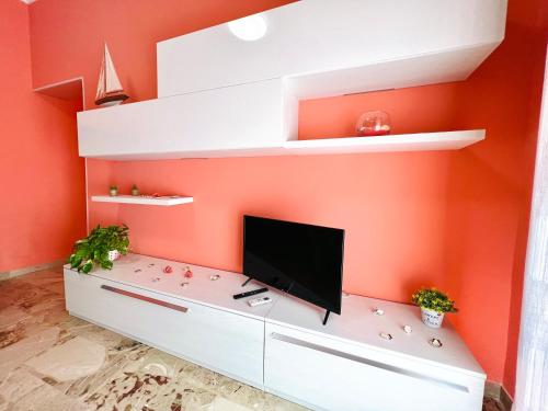 a living room with an orange wall with a tv and shelves at Domus Aurea in Isola delle Femmine