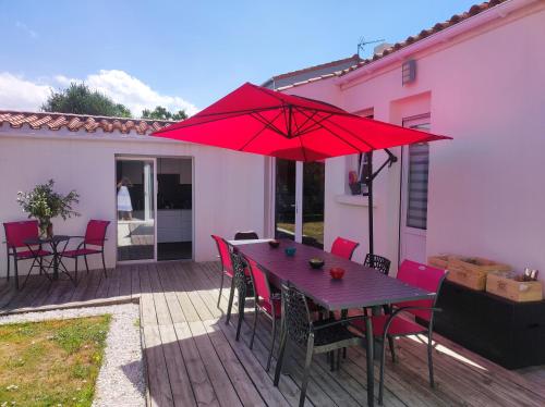 una terraza de madera con una mesa y una sombrilla roja en Chambre et salle d'eau dans dépendance 20 m2, vélos, en Les Sables-dʼOlonne