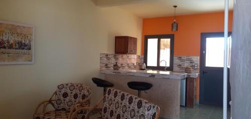 eine Küche mit orangefarbenen Wänden, einer Theke und Stühlen in der Unterkunft DEKK JAMM, où l'on trouve la paix in Toubab Dialao