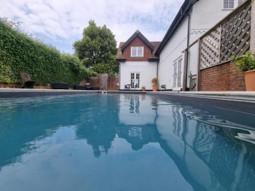 a swimming pool with blue water in front of a house at New Forest Cottage alongside Limewood Lyndhurst in Lyndhurst