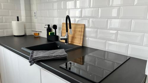 uma cozinha com um lavatório preto e azulejos brancos em Apartamenty Przy Deptaku em Świnoujście