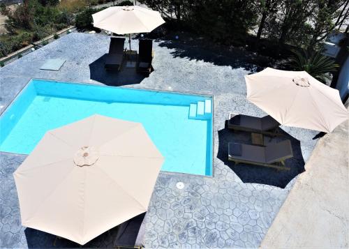2 weiße Sonnenschirme und ein Pool mit Tischen und Stühlen in der Unterkunft Villa Aurora Dome in Afandou