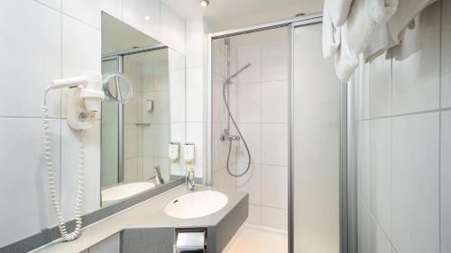 ein weißes Bad mit einem Waschbecken und einer Dusche in der Unterkunft Ringhotel Central - Superior in Rüdesheim am Rhein