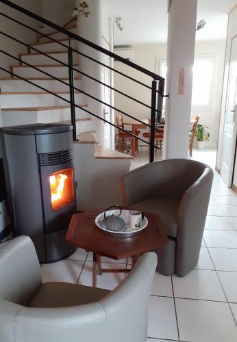 的住宿－Chambre coquelicots chaleureuse dans un écrin verdoyant，客厅设有壁炉、2把椅子和1张桌子