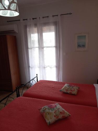 a bedroom with two beds with red sheets and a window at Elina Apartments in Batsi