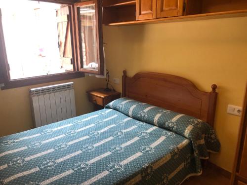 ein Schlafzimmer mit einem Bett mit blauer Decke und einem Fenster in der Unterkunft apartamentos casa botero in Sarvisé