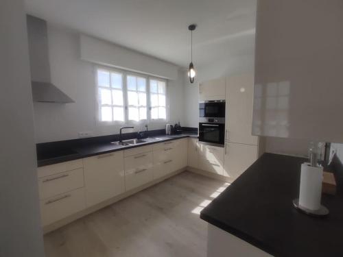 une cuisine avec des armoires blanches et un comptoir noir dans l'établissement Maison 7 pers. à 1km de la plage, à La Baule
