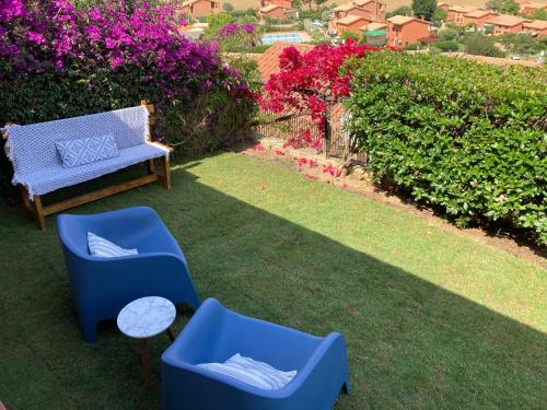 two blue chairs and a bench on a lawn with flowers at Villa Michela in Costa Rei