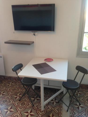 une table blanche avec quatre chaises et une télévision à écran plat dans l'établissement charmant studio Avignon intra muros, à Avignon