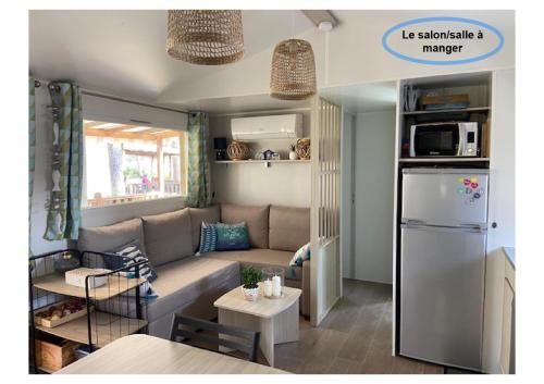 Elle comprend un petit salon doté d'un canapé et d'un réfrigérateur. dans l'établissement Charmant Mobilhome avec espace vert au milieu des pins proche de la plage sur le camping 