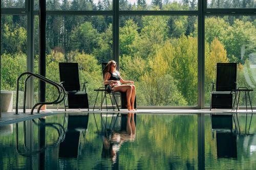 a woman sitting in a chair next to a swimming pool at Hotel Vyhlídka in Janske Lazne