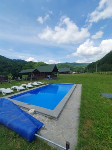 a swimming pool in a field with chairs and a house at Cabana Miraj in Groşii Ţibleşului