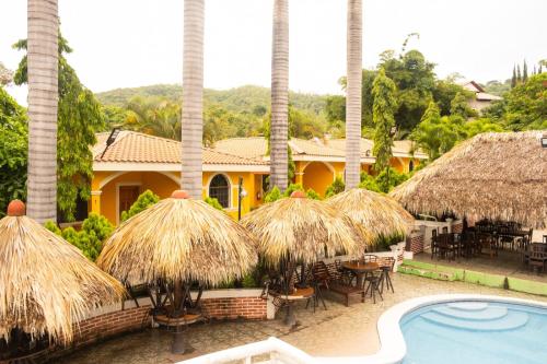 a resort with a pool and tables and straw umbrellas at Apart Hotel Acuarious de Luis in Estelí