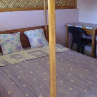 a bed with a wooden pole on it with a table at Bungalow le Charme, au bord de la mer in Marofarihy
