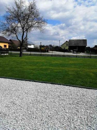 un campo de hierba con un árbol y una casa en Zatorska 113 - Zachwycający domek gościnny en Podolsze