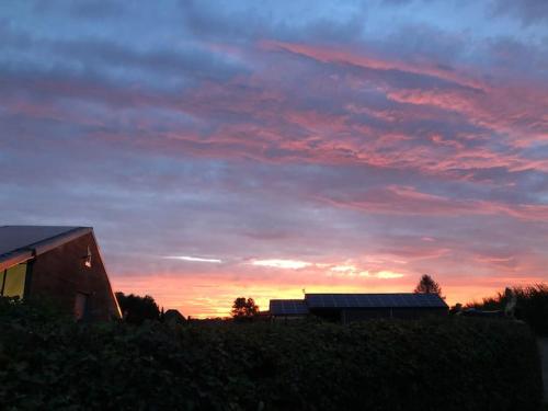 a sunset with a barn and a building in a field at Charming authentic renovated farm in Cadier en Keer