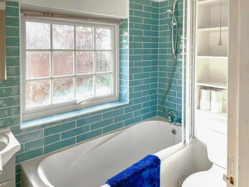 baño de azulejos azules con bañera y ventana en Garden Cottage 2 - Uk42882, en Liphook