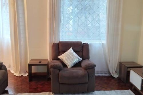 une chaise brune assise dans un salon avec une fenêtre dans l'établissement Stylish, Exquisite apartment in Nairobi, à Nairobi