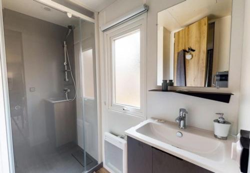 La salle de bains est pourvue d'un lavabo, d'une douche et d'un miroir. dans l'établissement Mobil home Lège Cap Ferret Camping 4 étoiles Les Viviers, à Lège-Cap-Ferret
