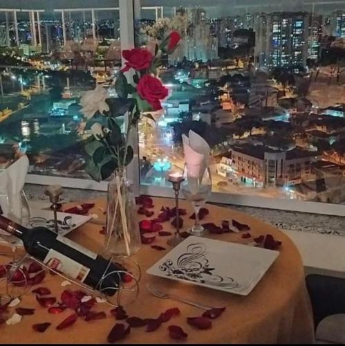 a table with roses in a vase and a window at Terraço Harmony Flats GRU in Guarulhos