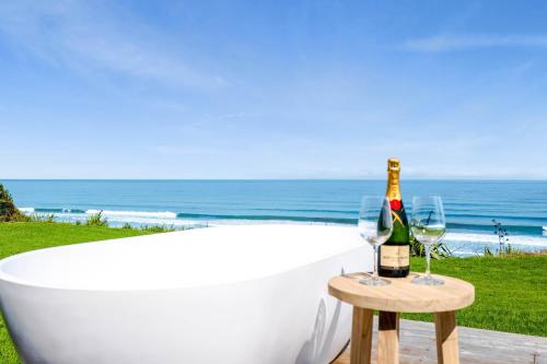 a bath tub with a bottle of champagne and two glasses at MOKAU BEACH HOUSE in Mokau