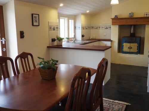 a dining room with a wooden table and a kitchen at Cobblers Cottage B&B in Willunga