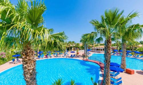 een zwembad in het resort met palmbomen en stoelen bij Villetta sul mare in Resort Village in Campofelice di Roccella