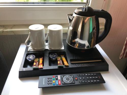 a coffee pot and two mugs and a remote control at MyCompass Hotel Offenbach in Offenbach