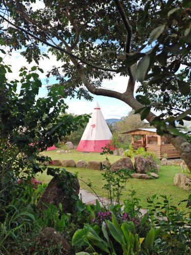 a red and white tent in a field with a house at BIOSFERA LODGE GLAMPING tipi 2 personas in Oxapampa