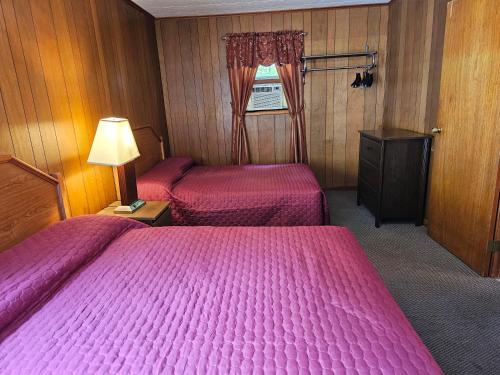 two beds in a room with pink sheets and a lamp at The Gold Eagle in Lake George
