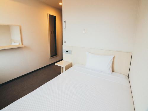 a bedroom with a white bed and a small cabinet at Quintessa Hotel Kokura Comic & Books in Kitakyushu