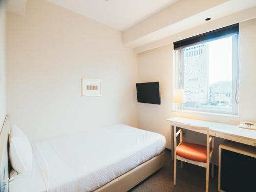 a bedroom with a bed and a desk and a window at Quintessa Hotel Kokura Comic & Books in Kitakyushu
