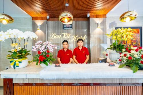 zwei Männer stehen hinter einem Tresen mit Blumen in der Unterkunft Bonka Hotel Luxury Quận 5 HCM in Ho-Chi-Minh-Stadt