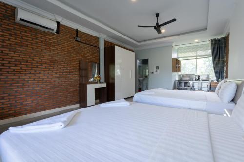 two white beds in a room with a brick wall at Sanssouci Kep in Kep