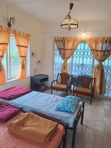 a bedroom with two beds and chairs and windows at Whispering Winds in Pune