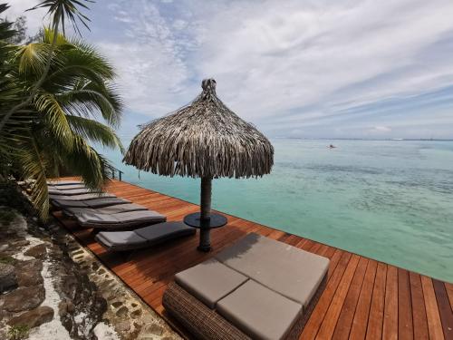 a deck with chairs and an umbrella and the ocean at Hôtel Fenua Mata'i'oa in Papetoai