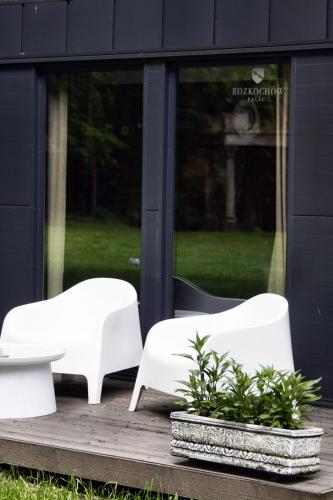two white chairs and a table in front of a building at Domki Hrabiego- domek nr 2 in Rozkochów