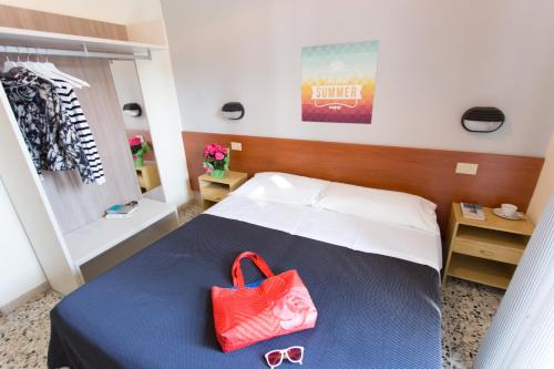 una camera da letto con un letto con una borsa rossa e occhiali da sole di Hotel Byron solo per giovani a Riccione