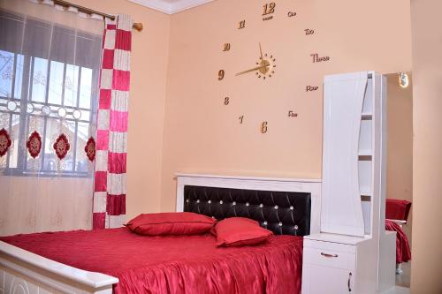 a bedroom with a bed with red sheets and a clock on the wall at Stunning 2-Bed Apartment in Namugongo Town Kampala in Kasiyirize
