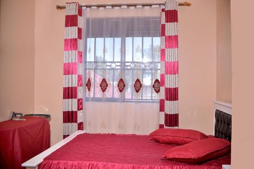 a bedroom with a red bed with a window at Stunning 2-Bed Apartment in Namugongo Town Kampala in Kasiyirize