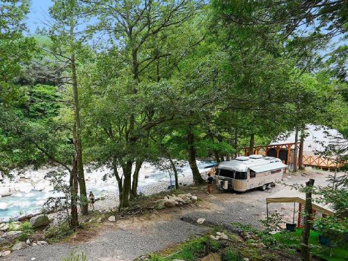 a camper parked next to a river with trees at リバーサイドグランピングNuts in Higashiomi