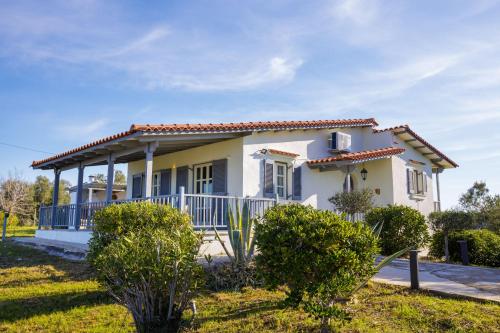 a white house with a porch and bushes at Villa Filokalia With Exceptional View - Happy Rentals in Kastro Kyllini