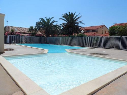 a large blue swimming pool with a fence and palm trees at Maison en bord de mer in Le Barcarès