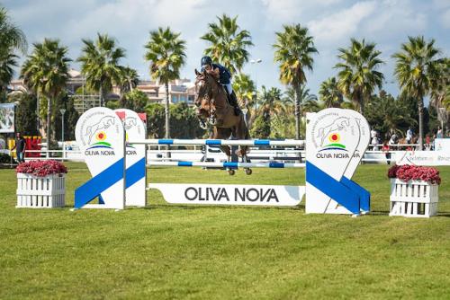 a person riding a horse jumping over an obstacle at OLIVA NOVA GOLF BEACH & RESORT club sevilla IV 2A in Oliva